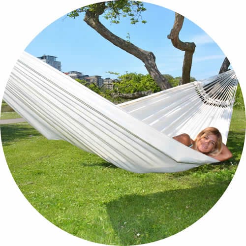 Kategori singelhängmattor symboliserad av en kvinna som ligger bekvämt och gungar i en naturfärgad hängmatta Bahia en park.